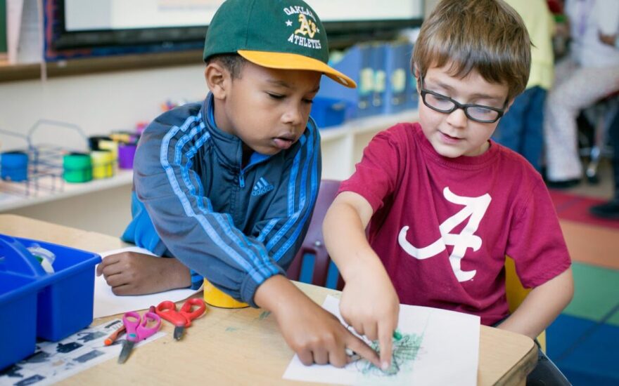 Two kindergarteners point at a drawing on a sheet of paper.