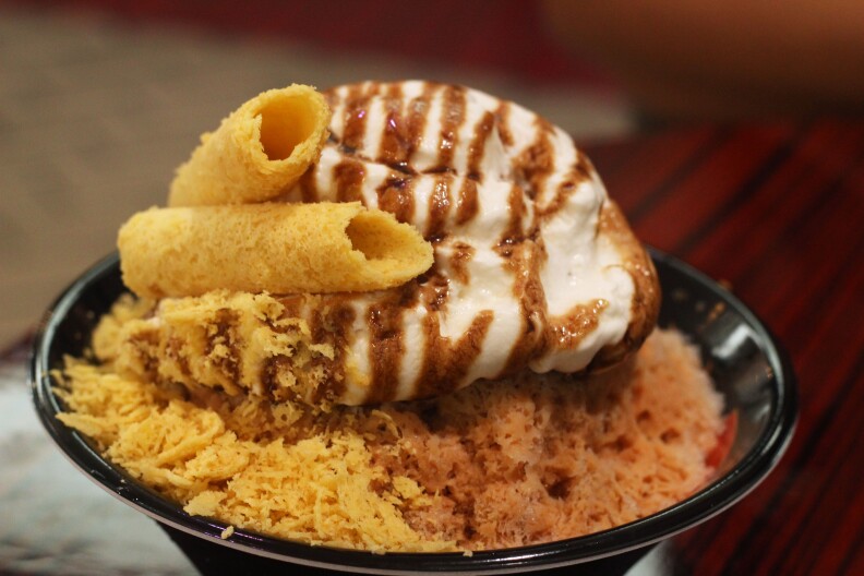 a gob of white cream drizzled with brown syrup on a mound of shaved cookie bits topped with two rolled cookies