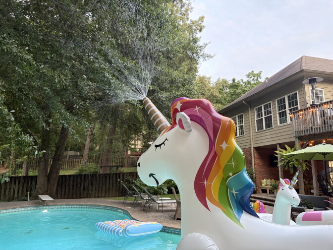 A large unicorn floatation device is seen in a pool with a two-story home in the background.