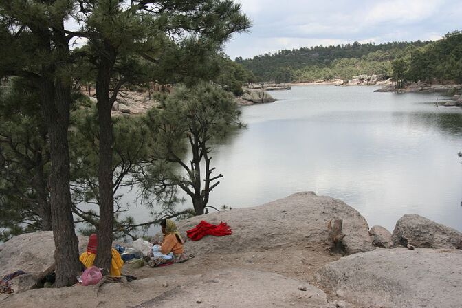 Two Tarahumara women (one with a baby nursing) at Arareco Lake near Creel, Chihuahua, Mexico. The Tarahumara are indigenous people of the Sierra Madre Occidental mountains in the state of Chihuahua in Mexico. The Tarahumara women wear the traditional brig