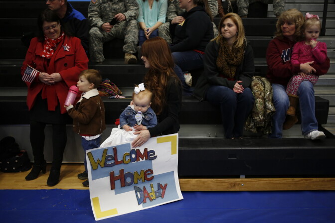 Army wife  (C) holds her daughter Annalise and a welcome home sign while waiting to greet her husband Spc. Eric Henry of the U.S. Army's 3rd Brigade Combat Team, 1st Infantry Division, during a homecoming ceremony in the Natcher Physical Fitness Center on Fort Knox on February 27, 2014 in Fort Knox, Kentucky. About 100 soldiers returned to Fort Knox after a nine-month combat deployment conducting village stability operations and working alongside Afghan military and police forces.