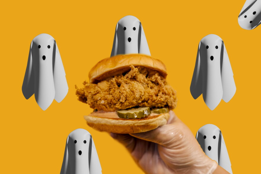 A hand in a latex glove holds up a fried chicken sandwich. Behind it are white ghosts with surprised faces against an orange-yellow background.