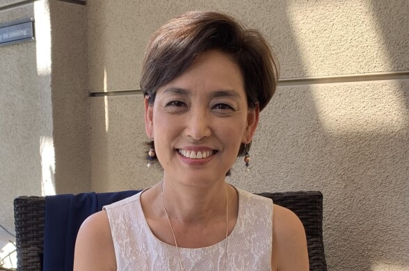 A Korean American woman in a white sheath poses in a chair.