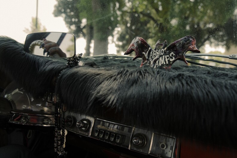 A figurine of a black bat with the words "Varrio Vamps" sits on top of a car's dashboard that is covered in black fur.
