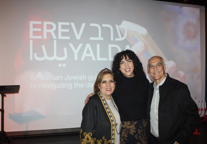 A female presenting person with dark, curly hair stands next two two older persons.