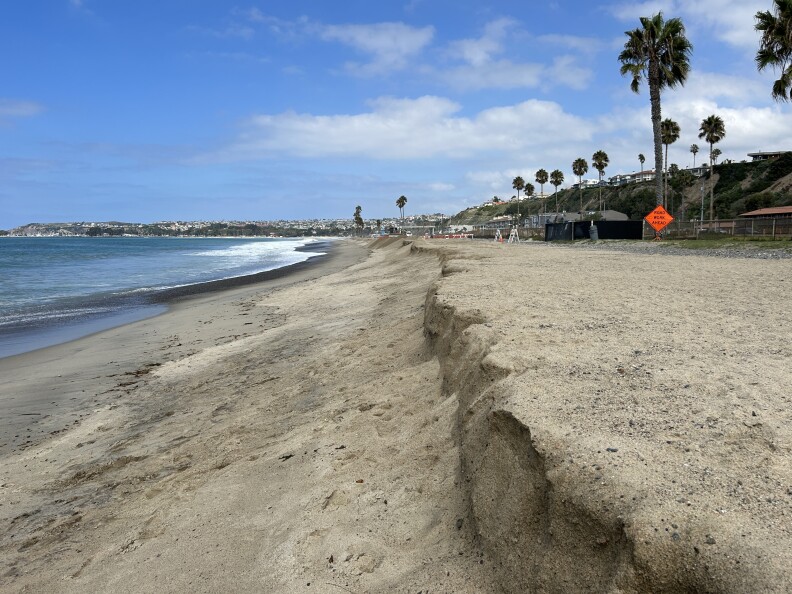 A long view of a sandy stretch of beach, where there's a dramatic fall off in the sand, a sign of how much erosion has taken place here.