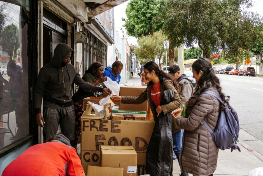 Several people stand on the sidewalk looking through a giant cardboard box labeled "Free Food."