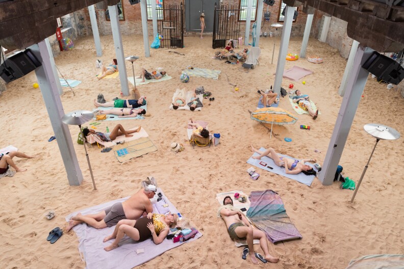 a bunch of people wearing swimsuits lay on towels on the sand inside a warehouse