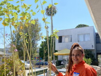 London Odom touches a more than one story tall sunflower at the Bel Air Guest Home in Hollywood. Odom wears a bright orange shirt and the sun is shining behind her. 