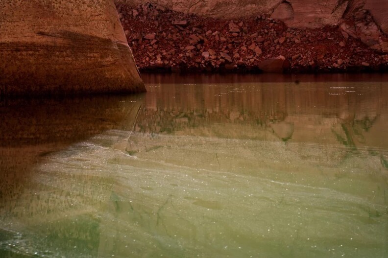 Water reflects red and brown shoreline dirt, along with green and yellow hillsides.