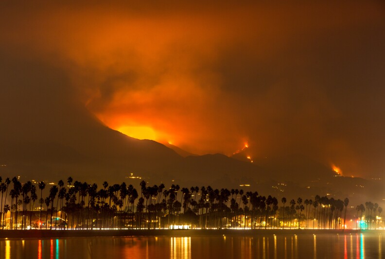 Fire, smoke, and ash are burning in the hills in the distance.