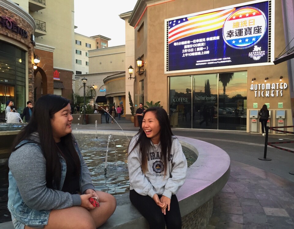 Two Asian people sit on the edge of a fountain near a ticket booth
