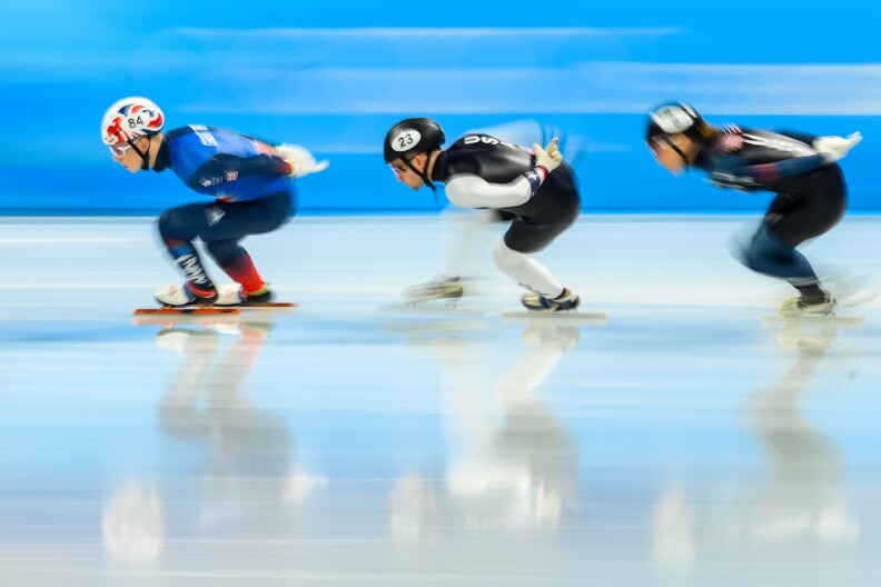 A line of three speedskaters in bent skating position, moving swiftly, the photo blurred.