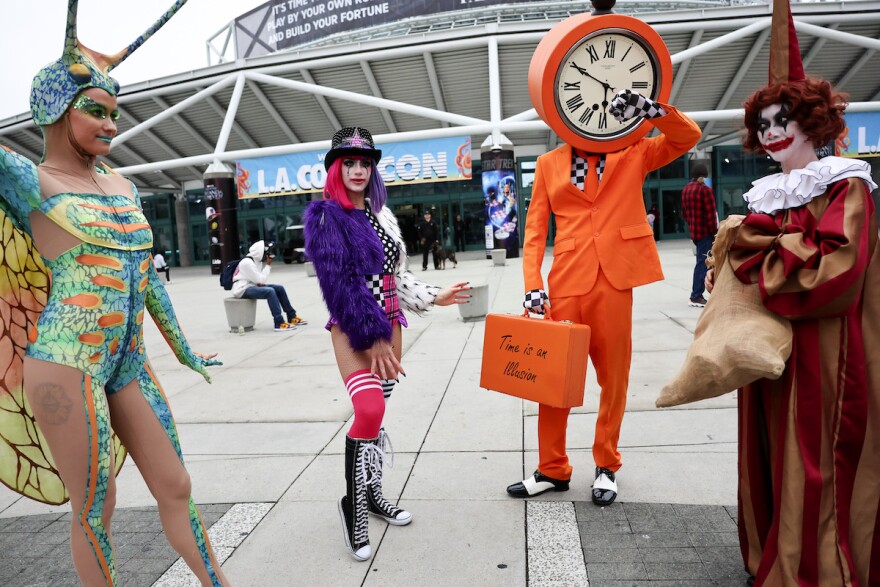 Four people dressed in extravagant, colorful costumes pose outside the Los Angeles Convention Center.