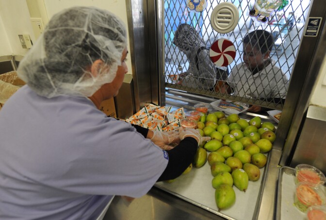 A school cafeteria worker hands out fruit and drinks to school children at the Normandie Avenue Elementary School in South Central Los Angeles on December 2, 2010.  First Lady Michelle Obama, a champion of measures to fight childhood obesity in the United States, welcomed passage in Congress Thursday of a law aimed at improving the quality of school meals. The House of Representatives earlier passed The Healthy, Hunger-Free Kids Act, following passage by the Senate. The bill now awaits President Barack Obama's signature to become law. It allows the federal government to encourage schools, through subsidies, to serve students meals that respect nutritional standards set by the National Academy of Sciences. Michelle Obama called the bill a "groundbreaking piece of bipartisan legislation that will significantly improve the quality of meals that children receive at school and will play an integral role in our efforts to combat childhood obesity.               AFP PHOTO/Mark RALSTON (Photo credit should read MARK RALSTON/AFP/Getty Images)