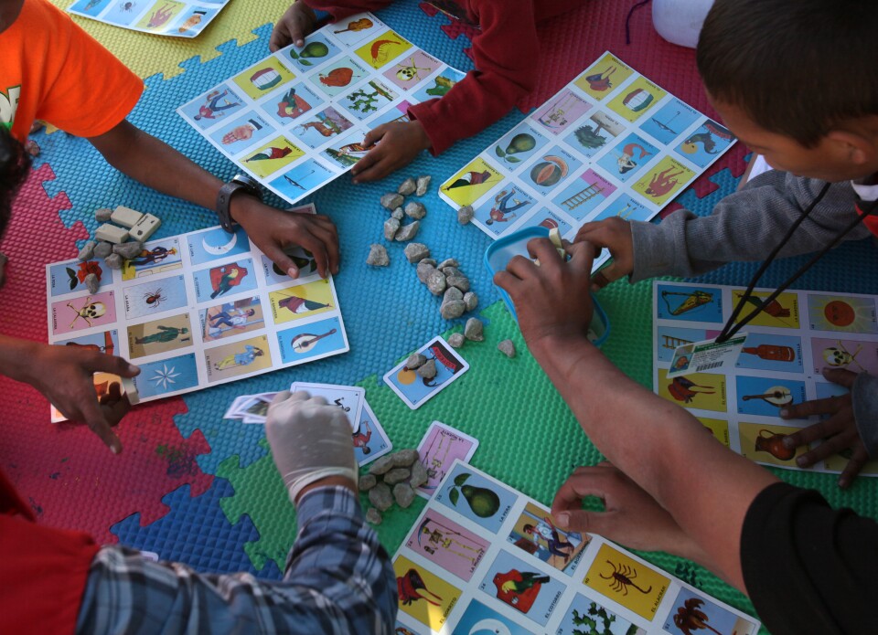 Tijuana, BAJA CALIFORNIA, Mexico - December 16:   At the El Barretal shelter in Matamoros, Tijuana, children play listeria with one of the workers at the Save the Children tent.

 In Tijuana, Mexico, children members of the migrant caravan are learning to live in limbo as they move between shelters, settling in as much as possible to create a sense of normalcy, with help from NGOs, counselors and aid organizations. (Photo by Peggy Peattie)