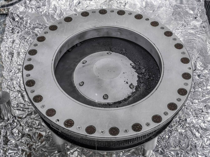 A ring-like object with a solid circle has debris in its center and in circle holes on the perimeter.