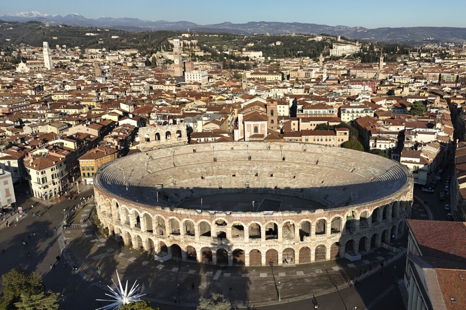 A large arena with arches and columns is set around a town with buildings with red tile roofs.