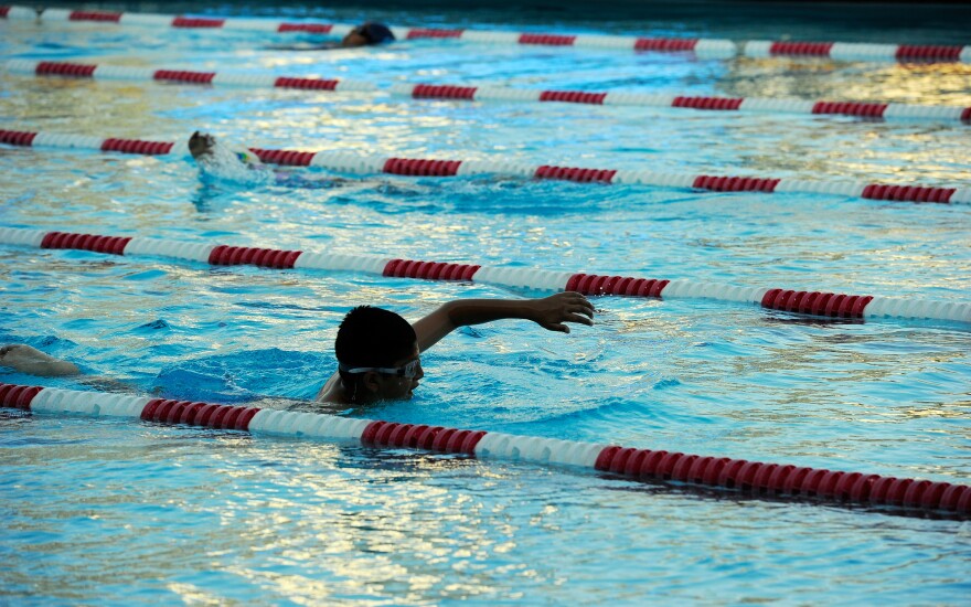 Three people are swimming in an indoor pool, separated by red and white barriers to mark individual lanes.