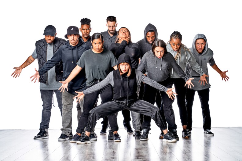 11 people wearing black pants and grey hoodies pose on a stage