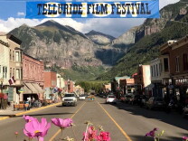 A main street in Telluride has a film festival banner stretched over the street with the mountains in the background