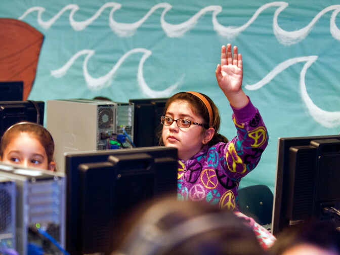 Third grader Natalia Gonzalez raises her hand as students take quizzes during a computer lab session.