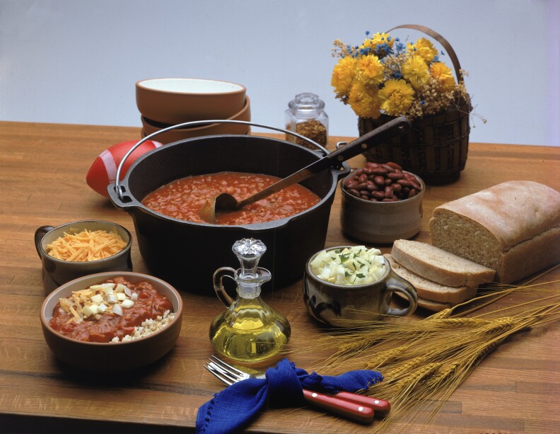 All the items necessary for a chili feast sit on a wooden surface.