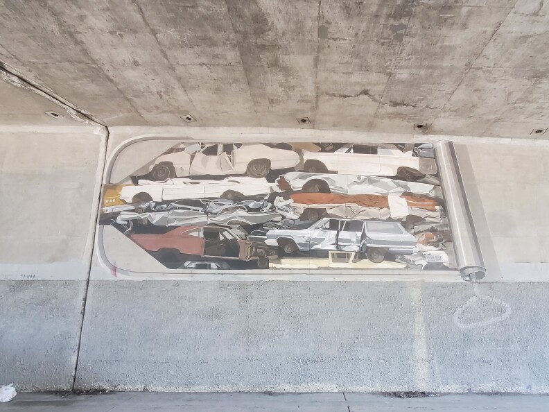 A mural on a wall underneath the 101 Freeway. It shows cars, piled up on top of each other, as if they are crammed into a sardine tin.