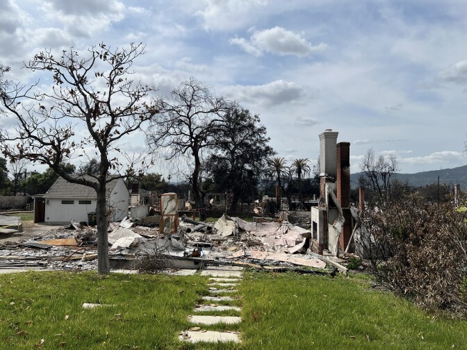 A house in ruins with a burned tree in front.
