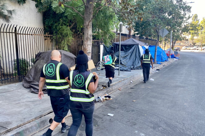 Four outreach workers from Urban Alchemy are walking down the street wearing all black and vests that identify them as part of Urban Alchemy, the nonprofit hired by Mitch O'Farrell's district to assist LAHSA with outreach. They are handing out food and water to unhoused people. 