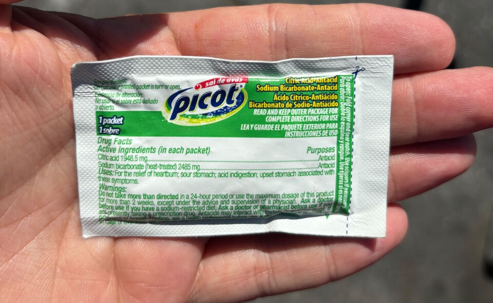 A light skin hand holds a white packet with a round logo with the words Picot in the middle. The rest of the corresponding writing contains drug facts and directions in light green lettering. 