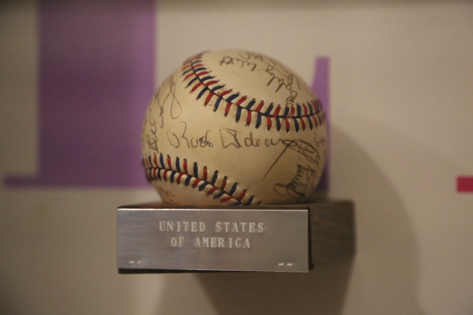 A baseball with multiple signatures on it from the 1984 Olympic team on woodblock with a silver metal plaque that says United States of America. 