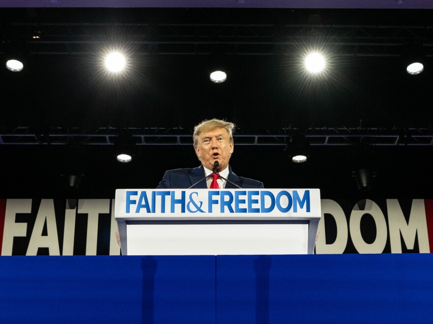 Donald Trump stands behind a lectern with the words Father & Freedom on it.
