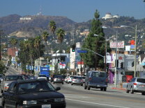 Sunset Blvd. in the daytime with cars and the Hollywood Sign and Griffith Observatory in the distance.