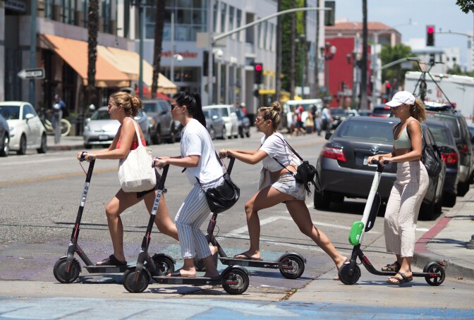 Young women ride shared electric scooters in Santa Monica, California, on July 13, 2018. - Cities across the U.S. are grappling with the growing trend of electric scooters which users can unlock with a smartphone app. Scooter startups including Bird and Lime allow riders to park them anywhere that doesn't block pedestrian walkways but residents in some cities, including Los Angeles, say they often litter sidewalks and can pose a danger to pedestrians. (Photo by Robyn Beck / AFP)        (Photo credit should read ROBYN BECK/AFP/Getty Images)