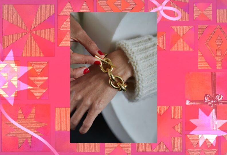 A close-up of a woman's hand putting on a bracelet, made of chunky, gold-chain links. The image is set against a festive turquoise background.