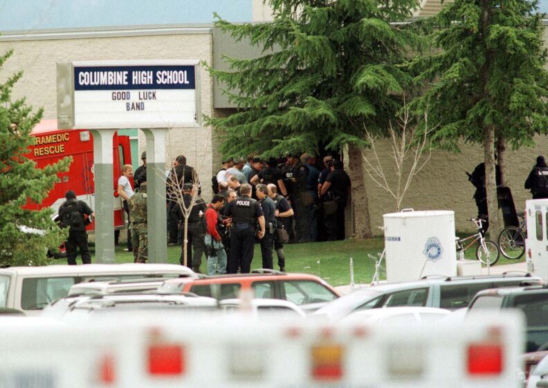 A sign reads: Columbine High School Good Luck Band more than a dozen law enforcement officers stand outside the school.