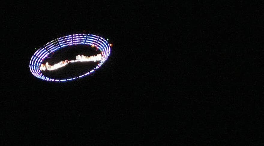 US plastic artist Peter Coffin's "Flying Saucer" --a 7-meter, LED-studded, SMS-controlled flying saucer and lifted by a helicopter-- overflies Ipanema beach, on May 23, 2009, in Rio de Janeiro, Brazil.  AFP PHOTO/Antonio Scorza (Photo credit should read ANTONIO SCORZA/AFP via Getty Images)