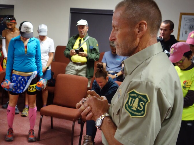                                In the minutes before the Angeles Crest 100 ultramarathon gets underway in Wrightwood, Martine Sesma, in blue, bows her head as U.S. Forest Service volunteer Gary Hilliard gives the invocation.