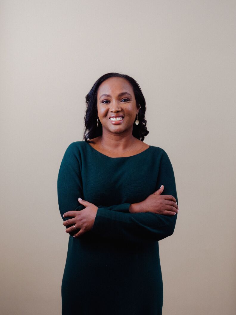 A portrait of a brown-skinned woman with her hands across her chest. 