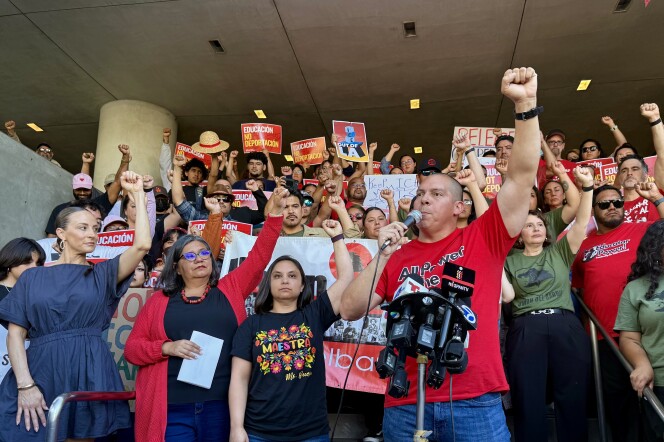 A group of people with varying skin tones raise their fists in the air. Many of them wear red shirts. Several people hold signs that say "educación, no deportación."