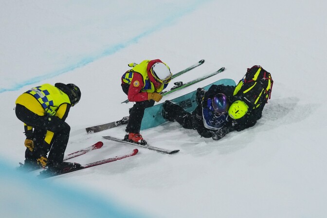 A snowboarder is on their side as two people come to their aid.