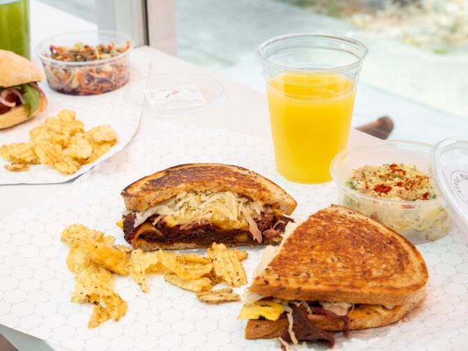 A partially eaten rueben sandwich sits on a counter in front of a window.