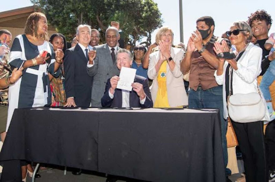 A photo of Gov. Newsom and others standing at a table he signed a bill giving back Bruce's Beach back to the family.