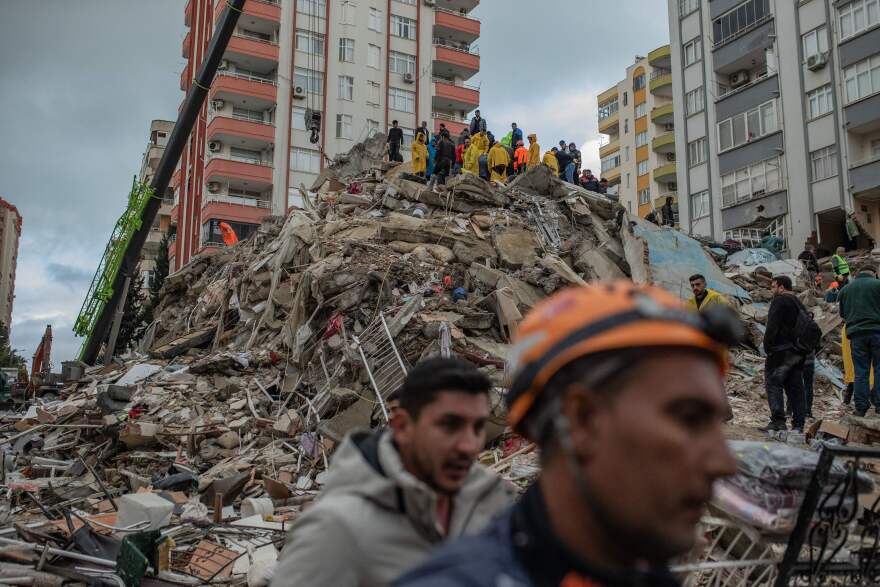 A collapsed building is being searched for survivors with a people atop a massive pile of rubble.