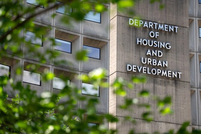 A large concrete building behind some green trees with a sign on the front that says "Department of Housing and Urban Development"