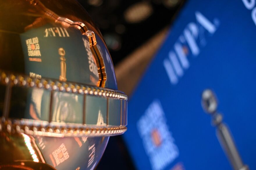 A shiny globe wrapped in a film reel reflects the HFPA logo and a screen promoting Golden Globe Awards.