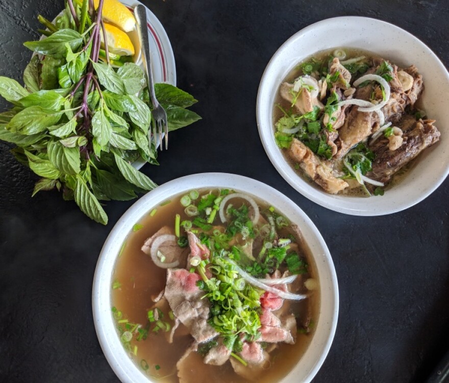 Two white bowls of the Vietnamese soup known as pho are seen from above, next to a small plate of garnishes.