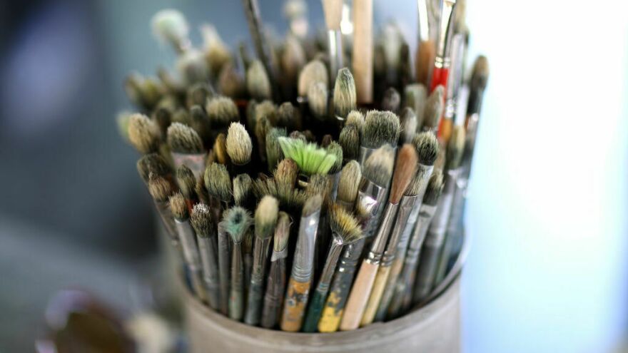 A cluster of paintbrushes is gathered in a container, with the brush tips pointed to the camera.