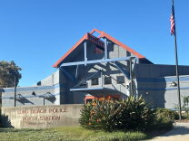 A concrete sign reads "Long Beach Police North Station" in front of a building with a peaked roof overhang and U.S. flag on a tall pole.